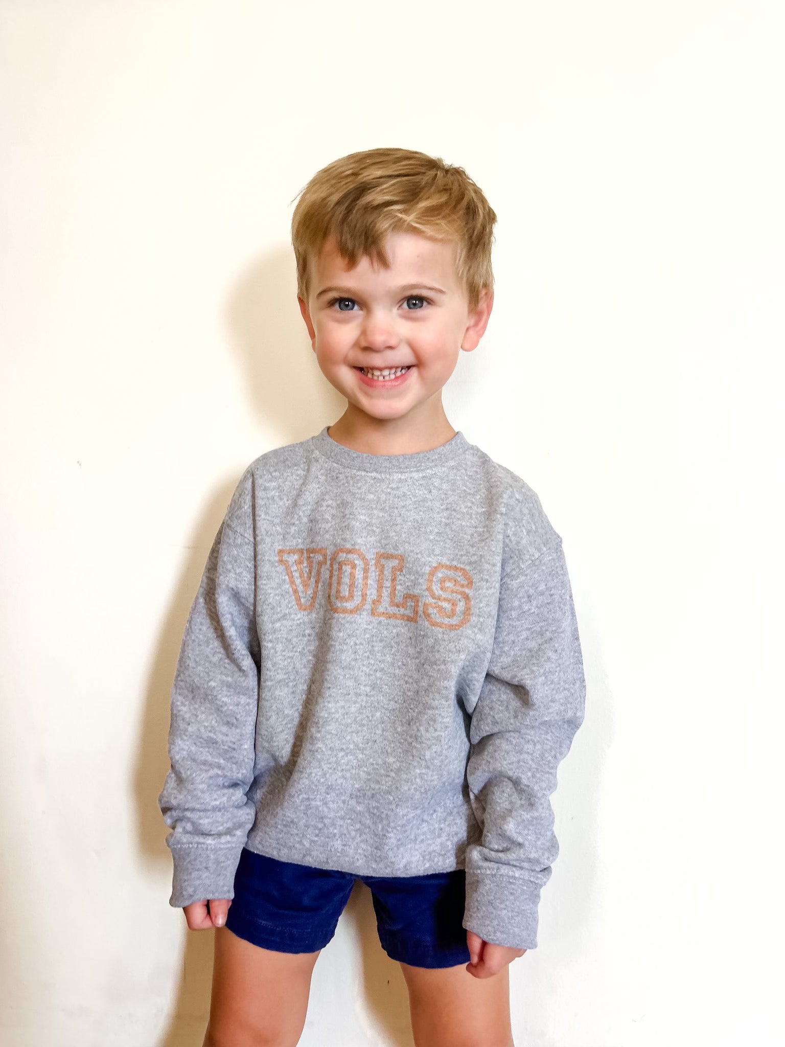 Child wearing a gray sweatshirt with 'VOLS' on a plain background